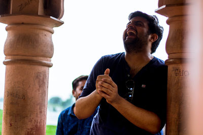 Low angle view of happy man standing by column against sky