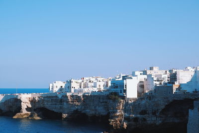 Buildings by sea against clear blue sky