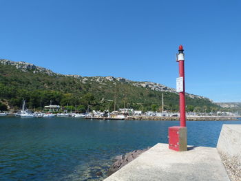 Lighthouse by sea against clear blue sky