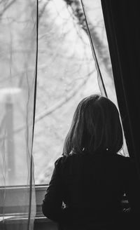 Rear view of girl looking through window