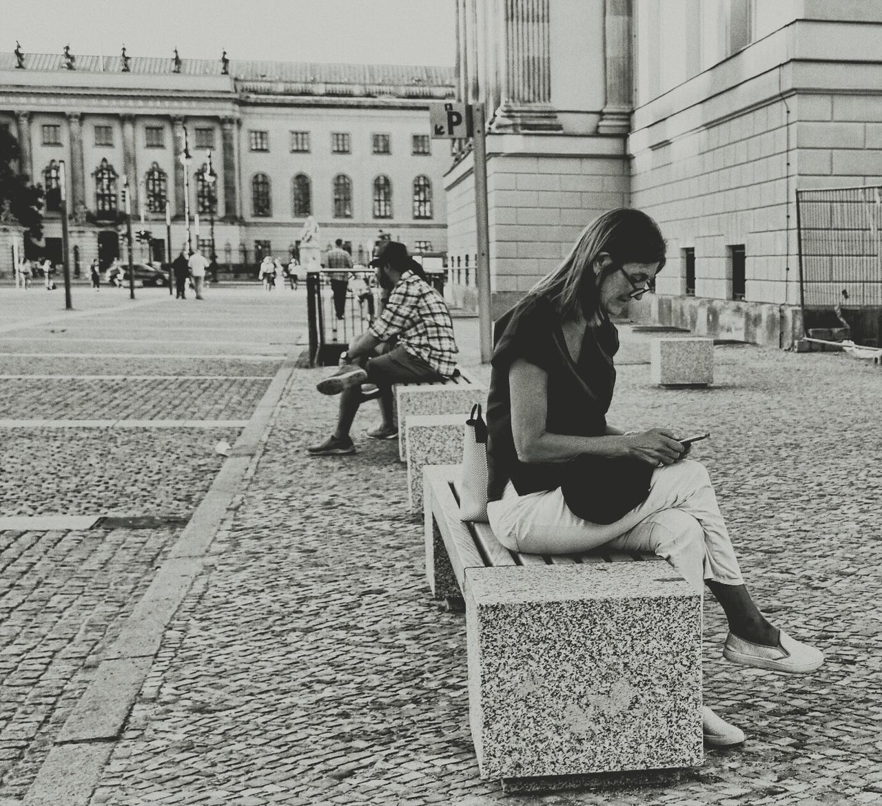 WOMAN SITTING ON STREET AGAINST BUILDINGS IN CITY