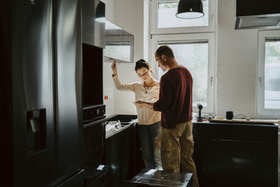 Couple discussing while fixing cabinet in kitchen during home renovation