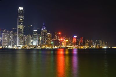 Illuminated buildings by river against sky at night