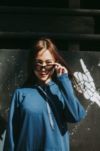 Portrait of young woman wearing sunglasses against wall