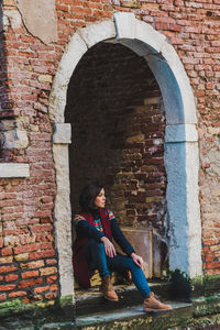 Full length of woman sitting against brick wall