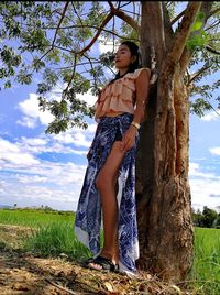 Low angle view of young woman standing on tree trunk in field