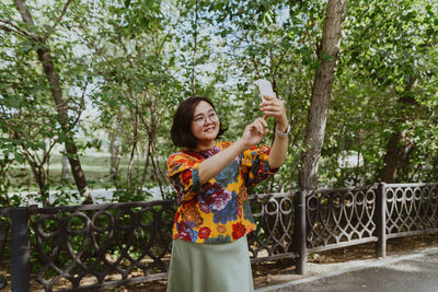 Brightly dressed woman with tech gadgets taking a selfie on sunny day in park