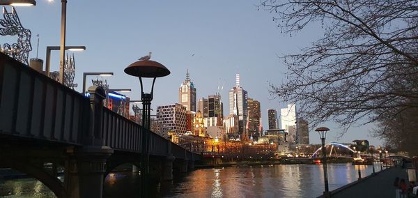 Bridge over river by buildings against clear sky