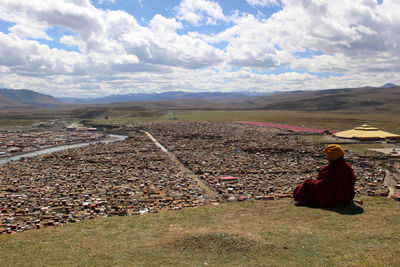 Rear view of man sitting on land against sky