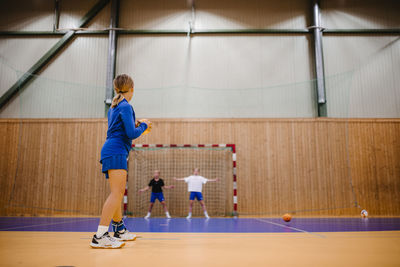 Side view of female handball player preparing to throw ball in sports court