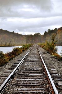 Railway tracks by lake against sky