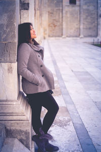 Woman looking away while leaning on wall