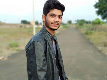 Portrait of young man standing on road against sky