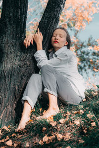 Woman sitting on grass by tree trunk during autumn