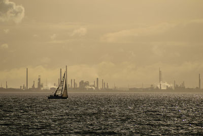 Sailboat sailing on river against cloudy sky