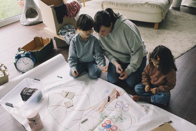 Mother with son and daughter drawing tree on cloth in living room at home