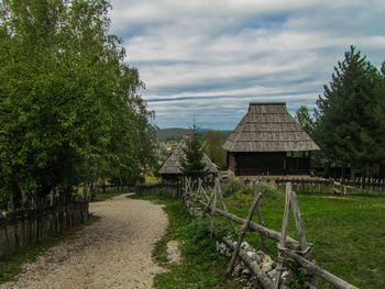 Empty walkway by grassy field against cloudy sky