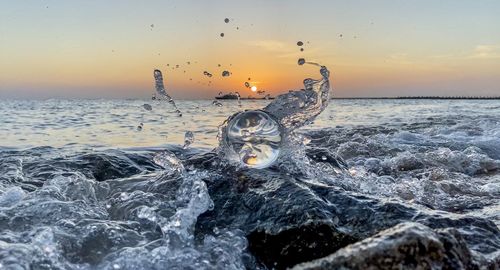 Water splashing in sea against sky during sunset
