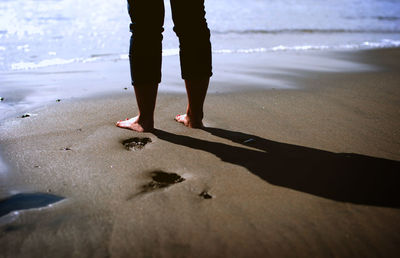 Low section of man standing on sea shore at beach