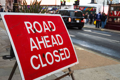 Temporary road ahead closed sign placed on sidewalk with city traffic