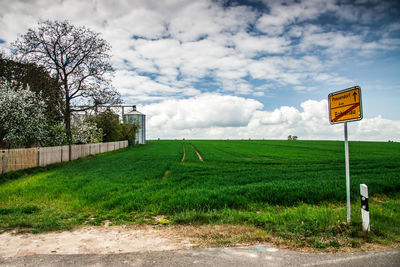 Road sign on field against sky