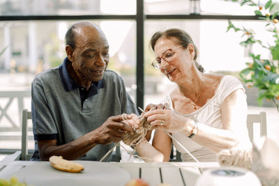 Senior woman teaching crochet to male friend at nursing home