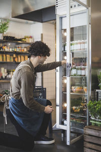 Young male owner taking bottle from refrigerator at store