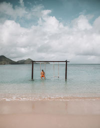 Man sitting on swing at beach against sky