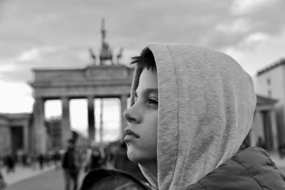 Close-up of thoughtful boy looking away against sky in city