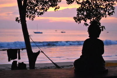 Silhouette statue at beach against sky during sunset