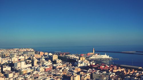 High angle view of townscape by sea against clear blue sky