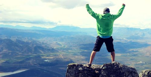 Rear view of man standing on rock against mountains