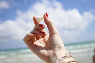 Cropped hand holding seashell at beach against sky