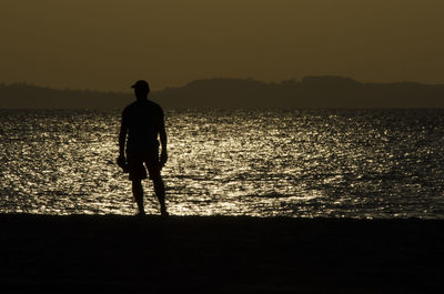 Rear view of silhouette man standing at beach during sunset