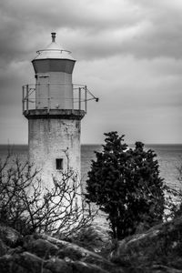 Lighthouse by sea against cloudy sky
