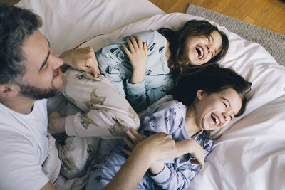 Happy father with playful daughters on bed at home