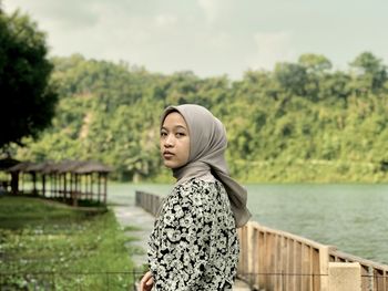Portrait of young woman standing against lake