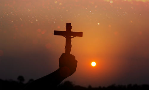 Cropped hand of man holding light against orange sky