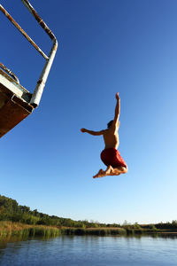 Low angle view of man jumping against clear blue sky