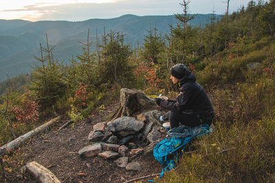 Outdoor wilderness trekking enthusiast sitting by a campfire enjoying breakfast at sunrise
