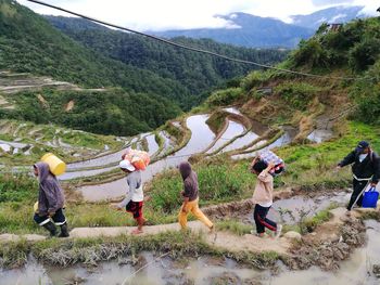 People standing on field by mountain against sky