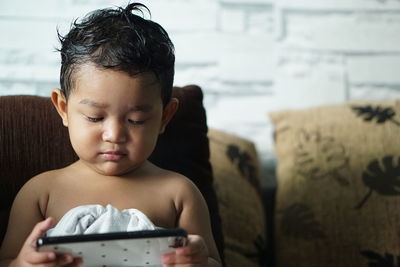 Shirtless baby boy holding mobile phone at home