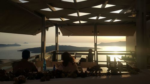 People sitting by sea against sky during sunset