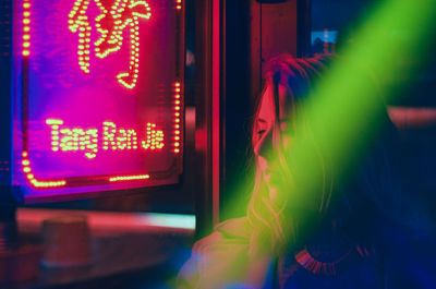 Close-up of young woman by illuminated neon sign at night