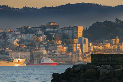 Sea by buildings against sky during sunset