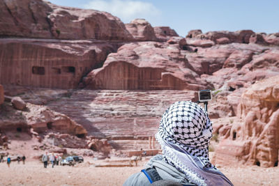 Rear view of woman taking selfie with camera wile standing against rock formation
