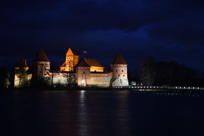 Illuminated buildings by river against sky at night