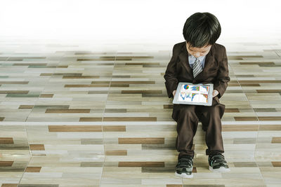 Boy in suit using digital tablet while standing on steps