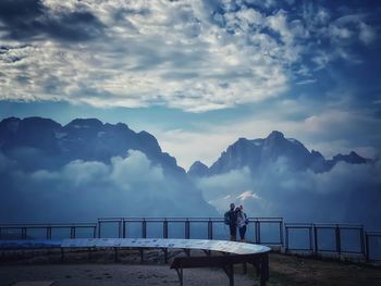 Men standing on railing against mountains against sky