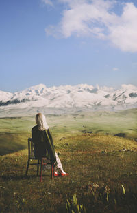 Woman sitting on chair while looking at view against cloudy sky